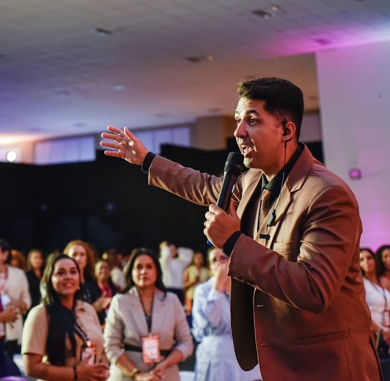 Hyago Nofre falando com a plateia de mulheres empreendedoras, braço estendido e microfone na mão